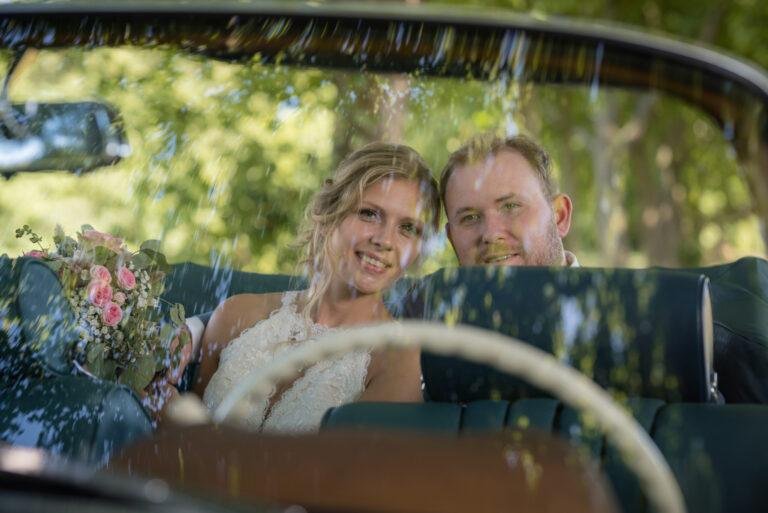 Brautpaar lacht im Oldtimer-Cabrio, Blick durch die Windschutzscheibe – Brautpaarshooting Miriam & Pascal
