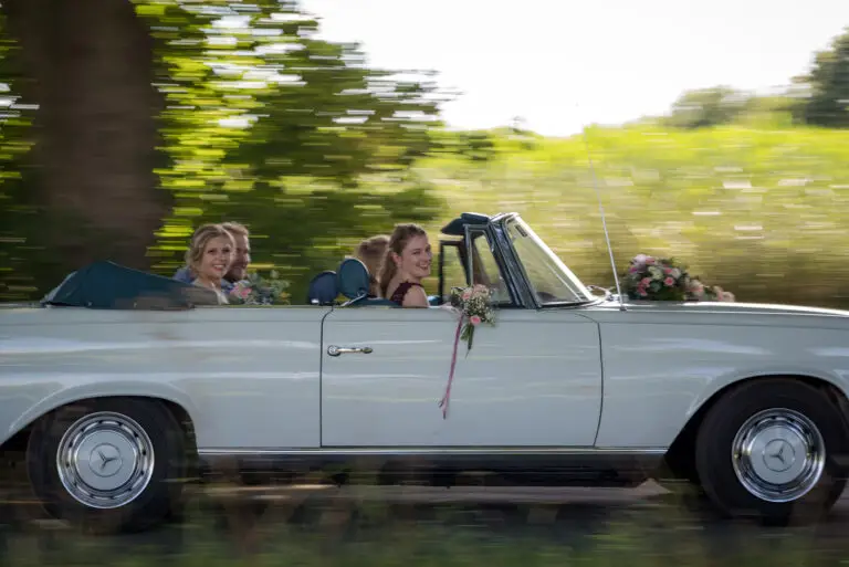 Weißes Oldtimer-Cabrio fährt mit dem Brautpaar durchs Grüne – Brautpaarshooting Miriam & Pascal