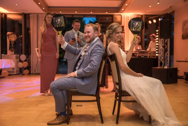 Brautpaar sitzt beim Hochzeitsspiel Rücken an Rücken auf Stühlen – Hochzeitsfeier Miriam & Pascal