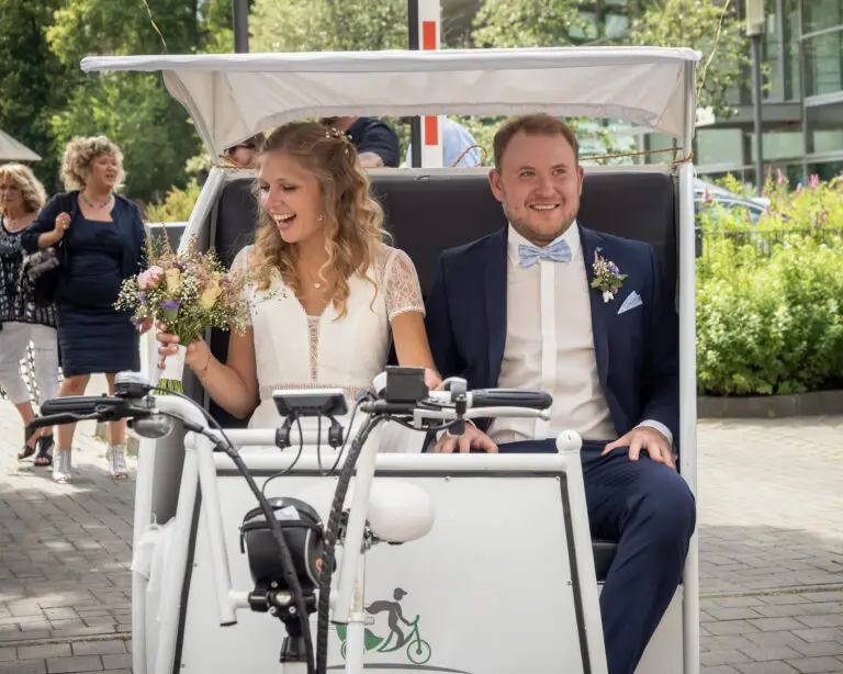 Brautpaar fährt lachend in einer weißen Rikscha – Hochzeit Miriam & Pascal