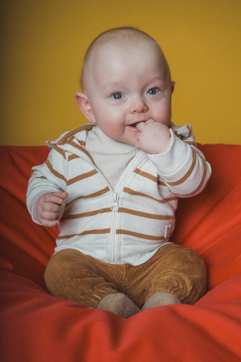 Baby sitzt vor gelbem Hintergrund auf einem roten Sitzsack – Babyfotos SNDR Photos Münster