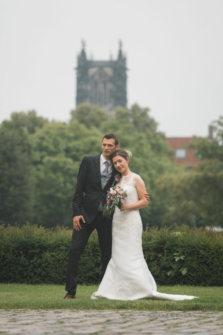 Web-13 Brautpaar vor einem Kirchturm im Hintergrund – Brautpaarshooting Bernadette & André am Schloss Münster