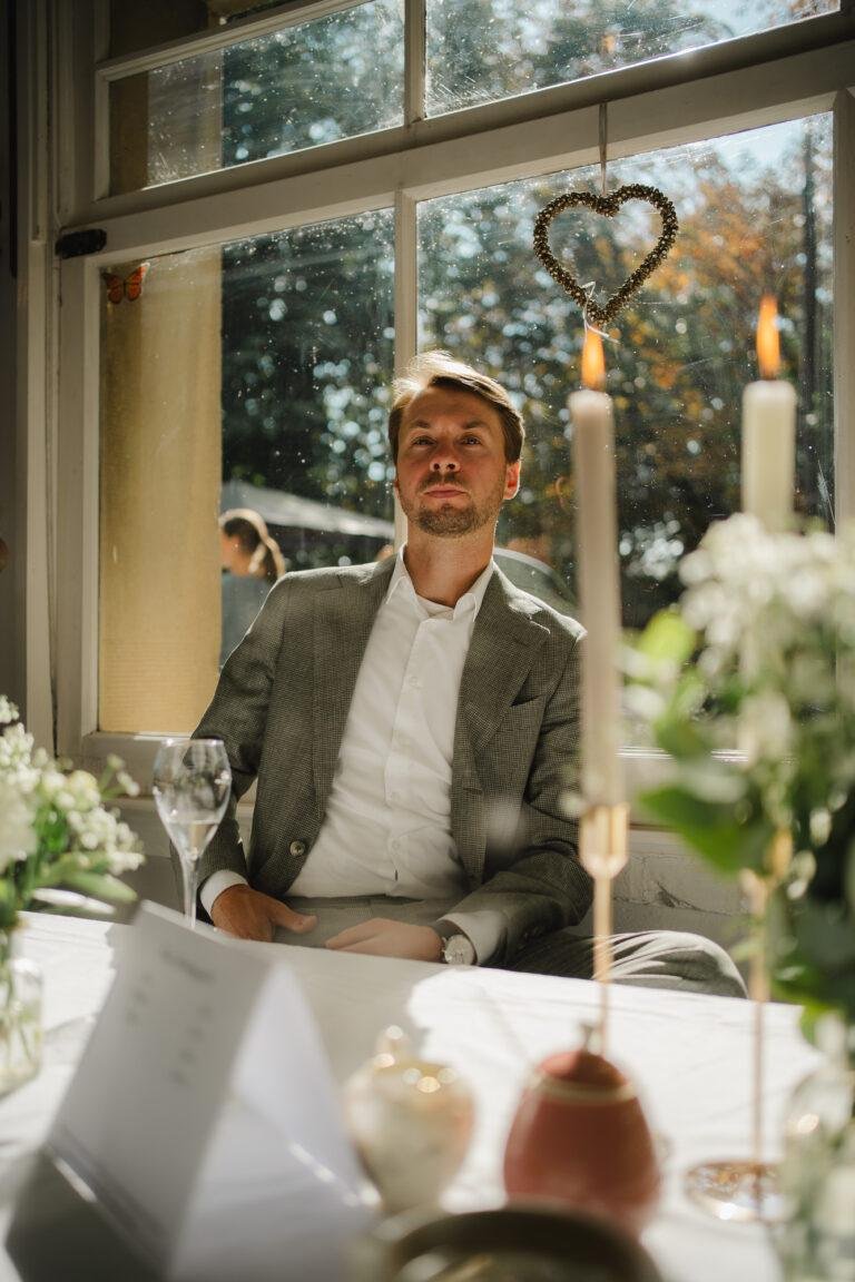 Web-18 Gast sitzt lachend am Fenster mit Kerzen – Hochzeitsfeier Renée & Patrick im Café Nobis