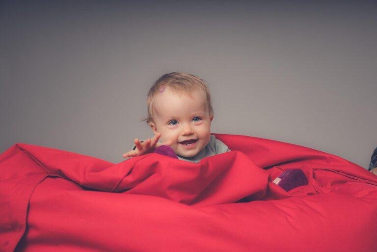 Baby liegt lächelnd in einer roten Decke – Babyfotos SNDR Photos Münster