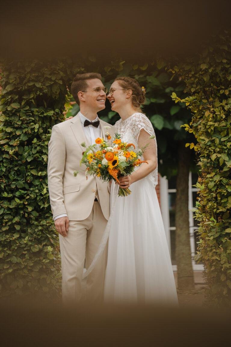 Brautpaar mit Brautstrauß vor einer grünen Hecke – Brautpaarshooting Nora & Simon
