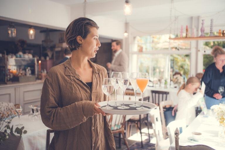 Web-21 Gast steht im hellen Café mit gedeckten Tischen – Hochzeitsfeier Renée & Patrick im Café Nobis