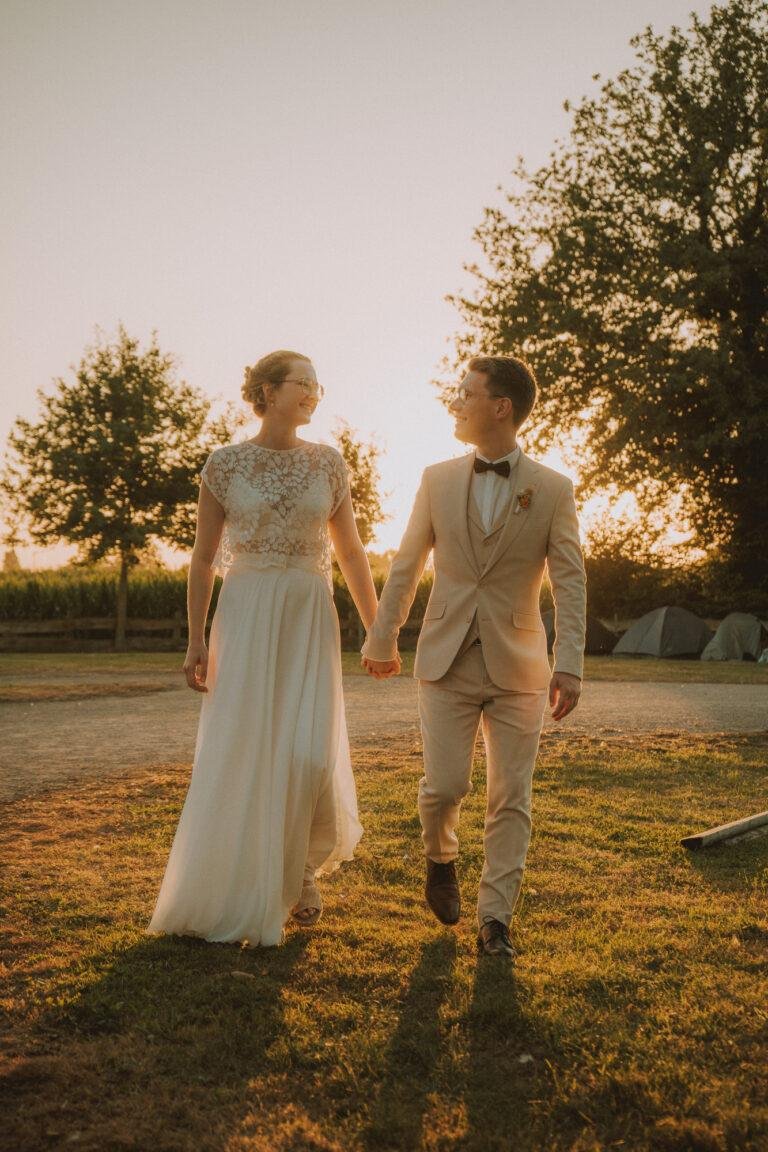 Brautpaar geht Hand in Hand im Sonnenuntergang über eine Wiese – Brautpaarshooting Nora & Simon