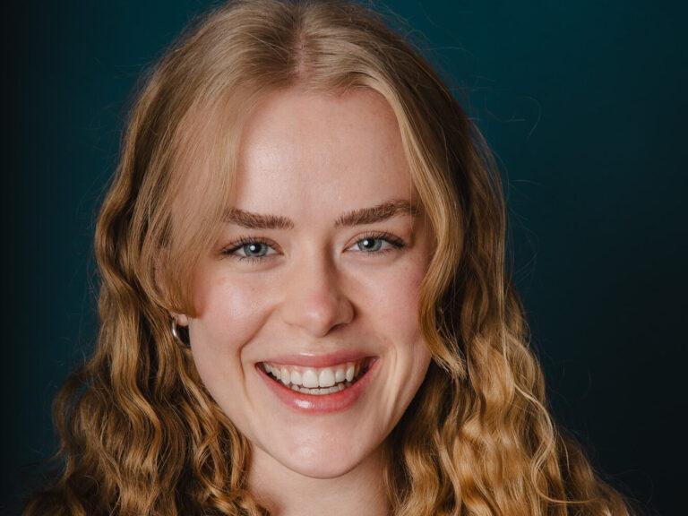 Junge Frau mit blonden Locken lächelt vor dunkelgrünem Hintergrund – Portraitfoto aus Münster