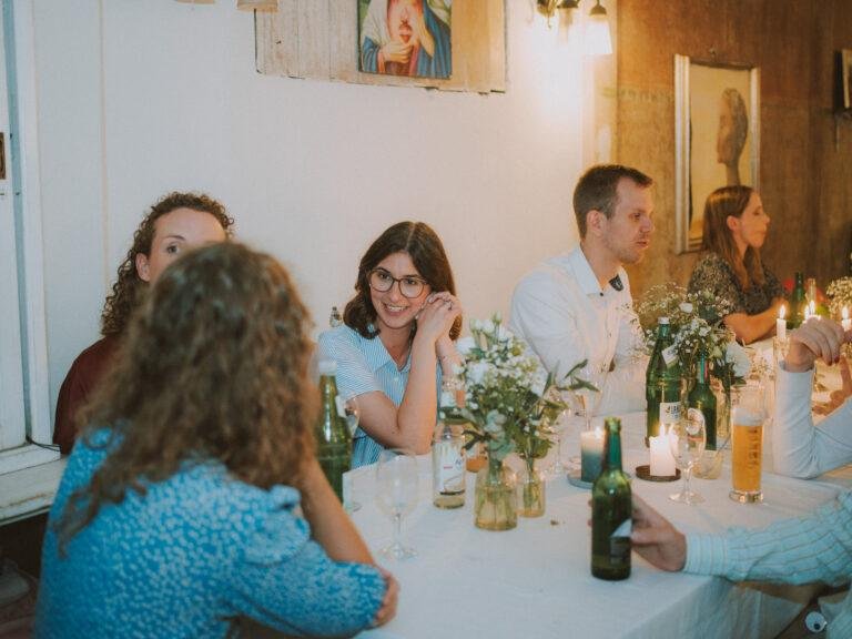 Web-31 Gäste sitzen lachend am festlich gedeckten Tisch – Hochzeitsfeier Renée & Patrick im Café Nobis