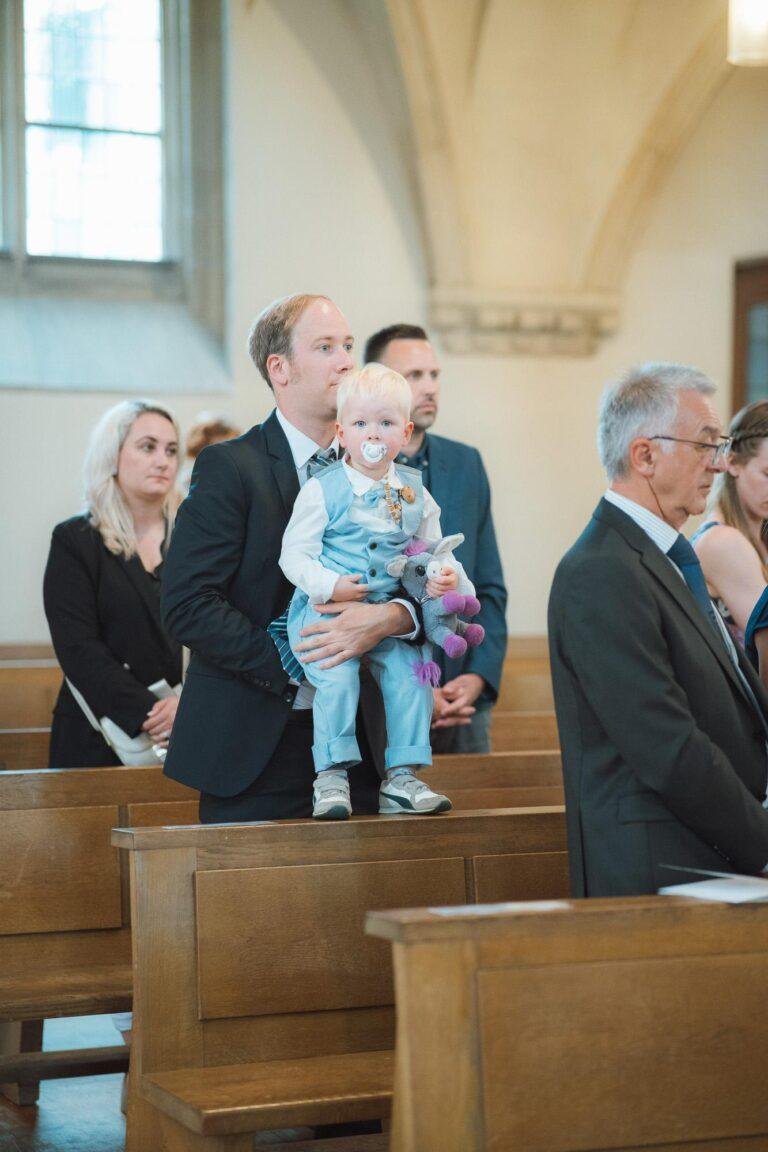 Web-34 Gast mit Kleinkind auf dem Arm in der Kirchenbank – kirchliche Trauung Bernadette & André