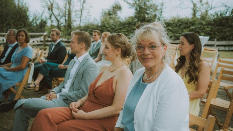 Hochzeitsgäste sitzen lächelnd bei der freien Trauung im Freien – Hochzeit Nora & Simon