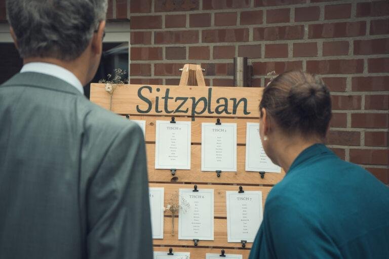Gast schaut auf den Sitzplan an der Backsteinwand – Hochzeitsfeier Nora & Simon