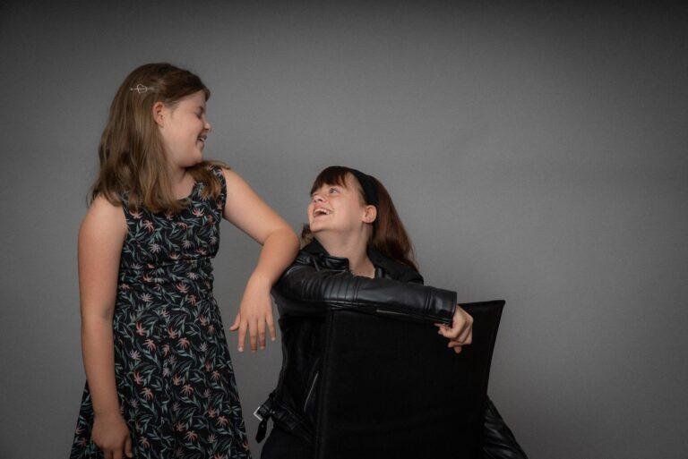 Zwei Schwestern lachen sich vor grauem Hintergrund an – Kinderfotos SNDR Photos Münster