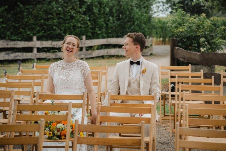 Brautpaar lacht zwischen den Holzbänken der Trauung – Brautpaarshooting Nora & Simon