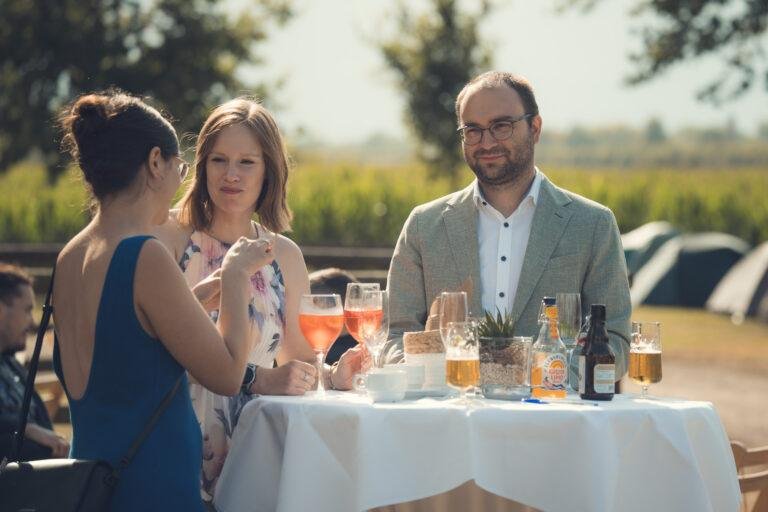 Gäste sitzen an einem Tisch vor einem Maisfeld – Hochzeitsfeier Nora & Simon
