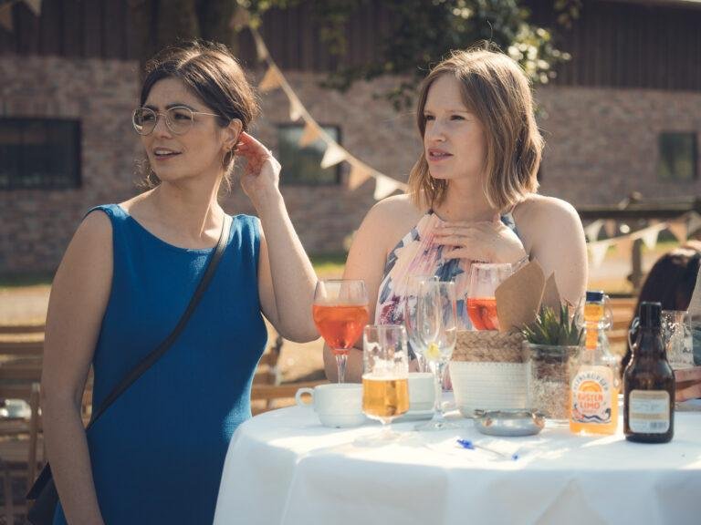 Zwei Frauen stoßen lachend am Tisch an – Hochzeitsfeier Nora & Simon