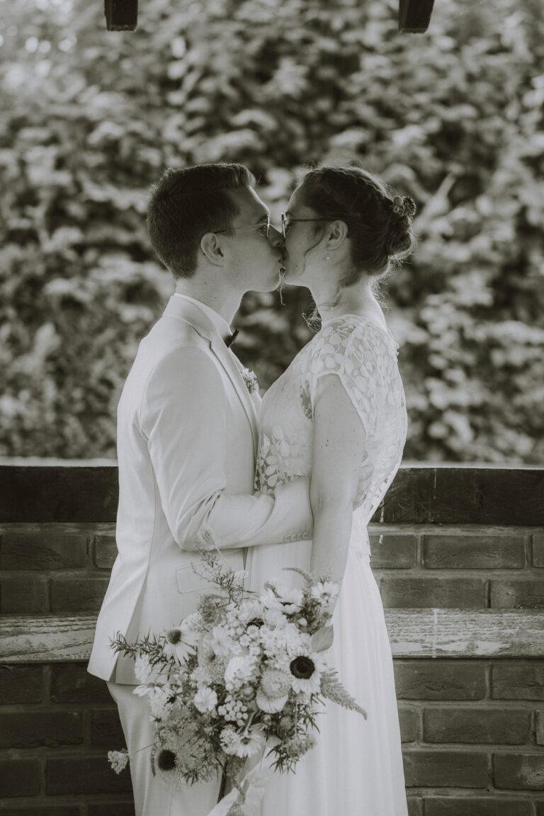 Schwarz-Weiß-Foto: Brautpaar küsst sich mit Brautstrauß – Brautpaarshooting Nora & Simon