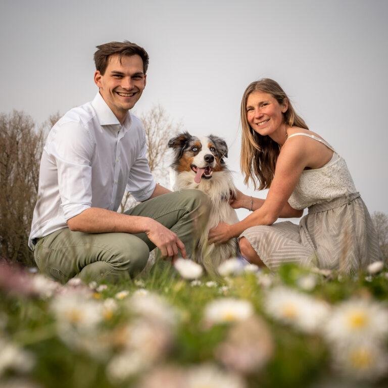 Paar sitzt mit seinem Hund zwischen Blumen auf der Wiese – Hundefotoshooting SNDR Photos Münster