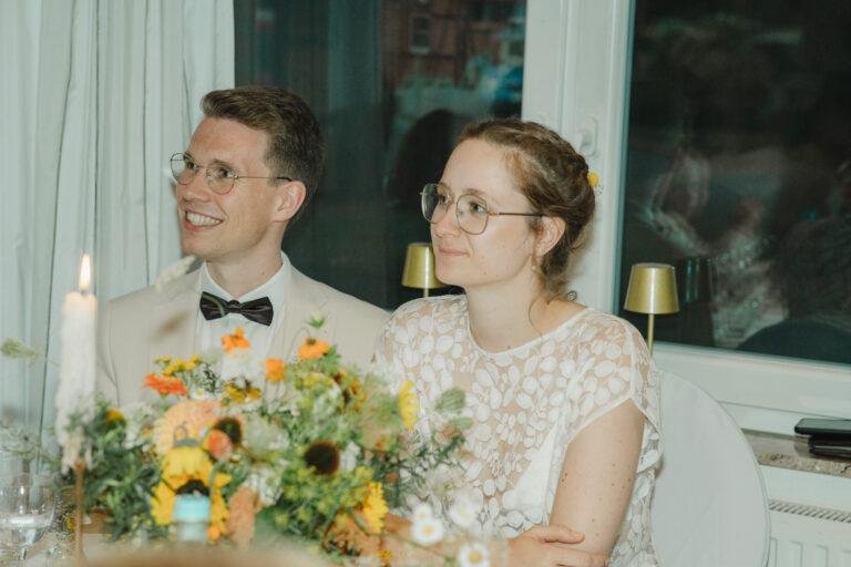 Brautpaar sitzt lächelnd am geschmückten Hochzeitstisch – Hochzeitsfeier Nora & Simon