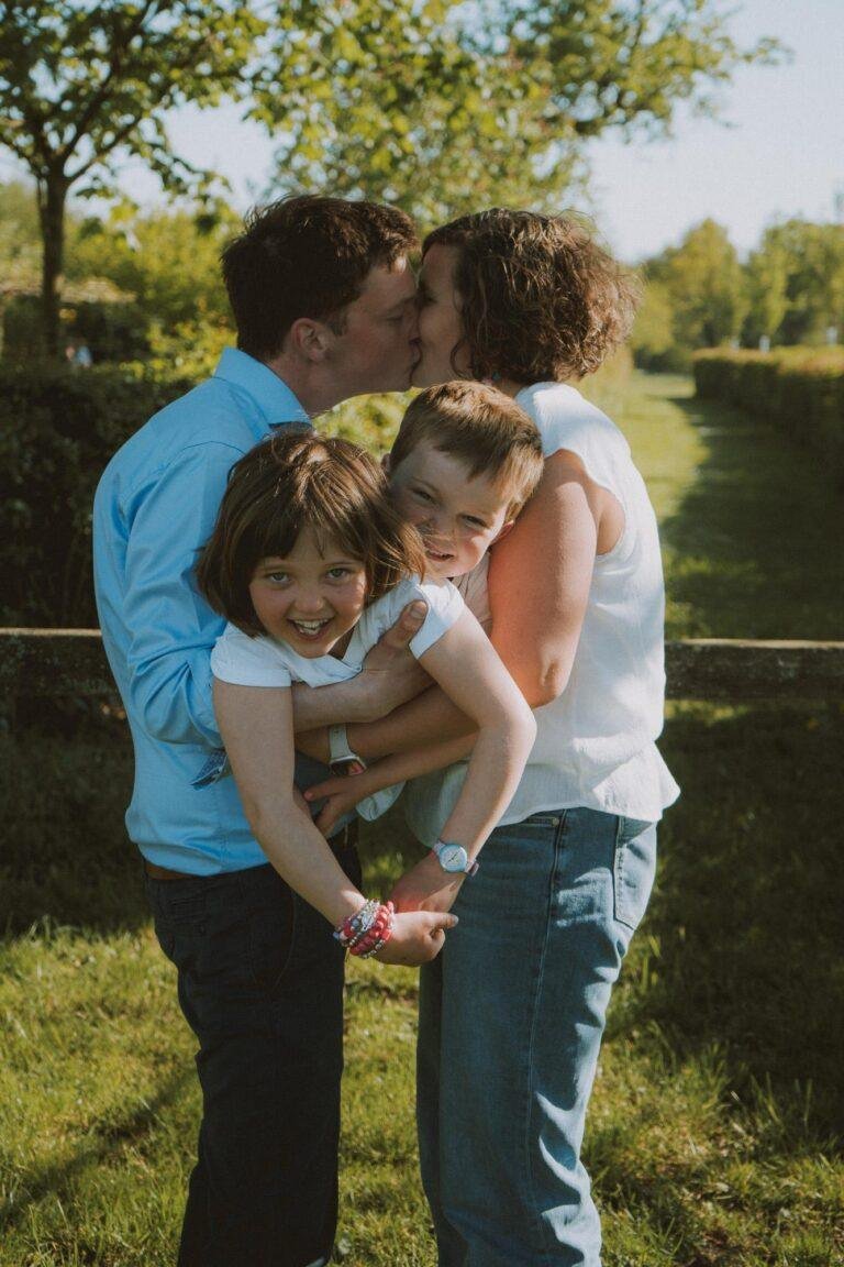 Eltern küssen sich, die Tochter auf dem Arm küsst mit – Familienfotoshooting SNDR Photos Münster