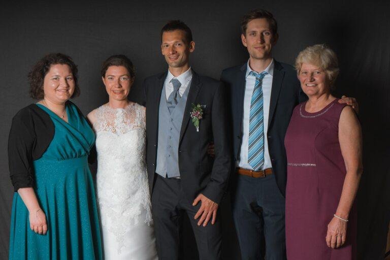 Web-78 Brautpaar mit Familie vor dunklem Hintergrund – Hochzeitsfeier Bernadette & André