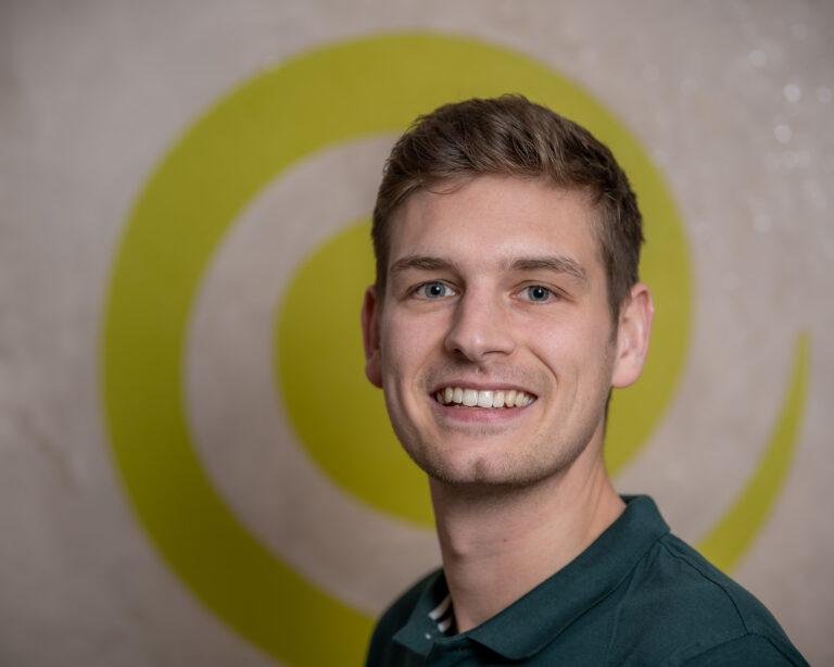 Mitarbeiter lächelt vor einem grünen Spiral-Logo – Business-Fotografie SNDR Photos Münster