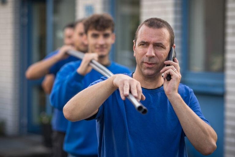 Handwerker im blauen Shirt telefoniert vor dem Firmengebäude – Business-Fotografie SNDR Photos Münster