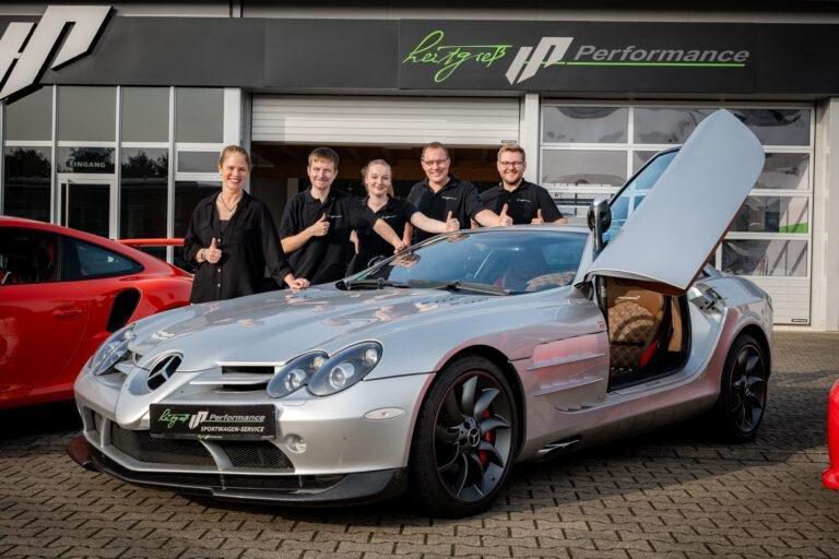 Team posiert neben einem silbernen Sportwagen mit Flügeltüren – Business-Fotografie SNDR Photos Münster