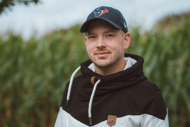 Mann mit Basecap und Hoodie lächelt vor einem Maisfeld – Dating-Fotos in Münster