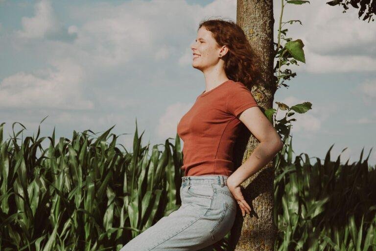 Junge Frau lehnt lächelnd an einem Baum am Feldrand – Uni-Abschluss Fotoshooting in Münster